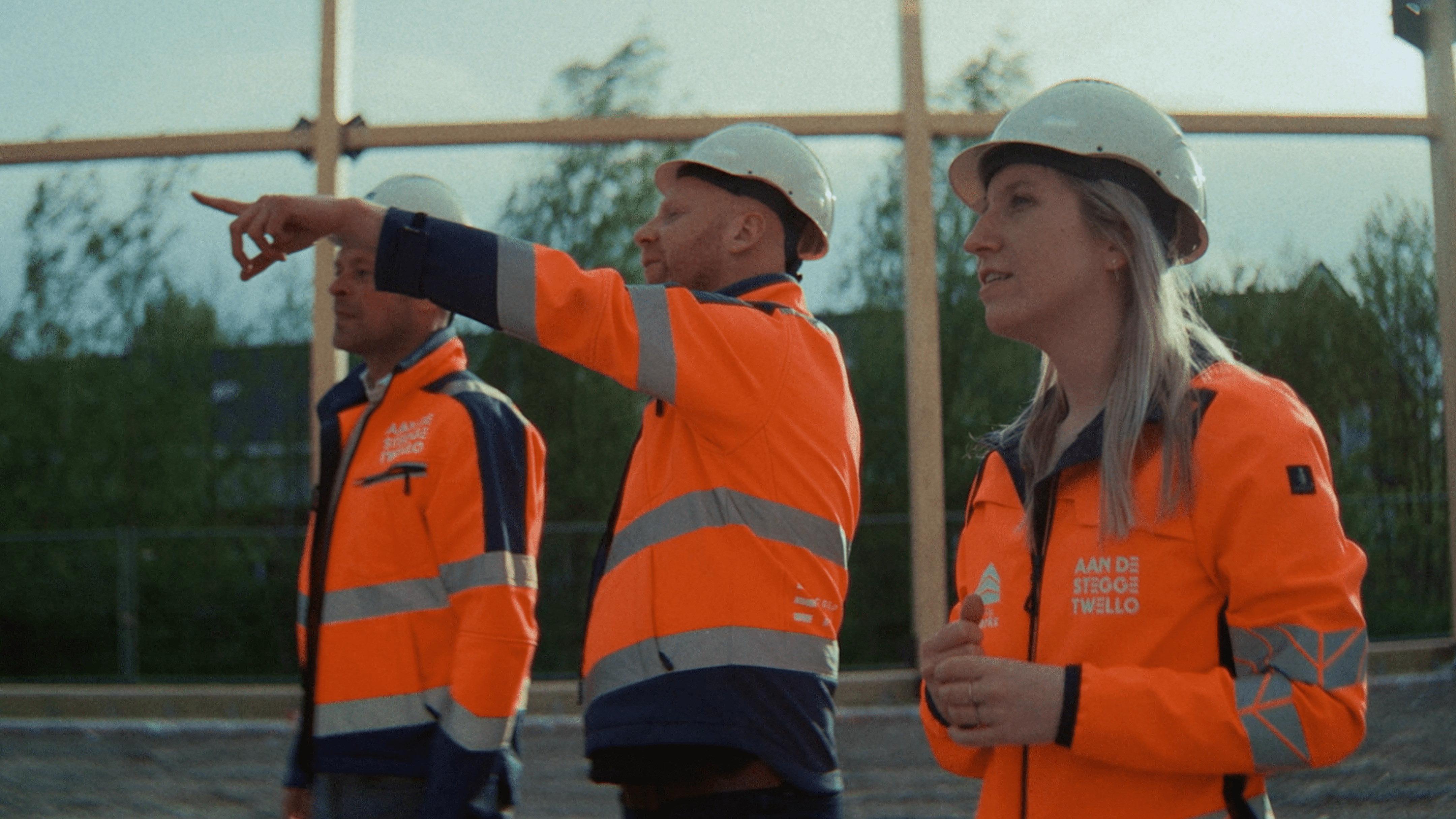 Drie bouwvakkers in oranje veiligheidskleding op een bouwplaats.