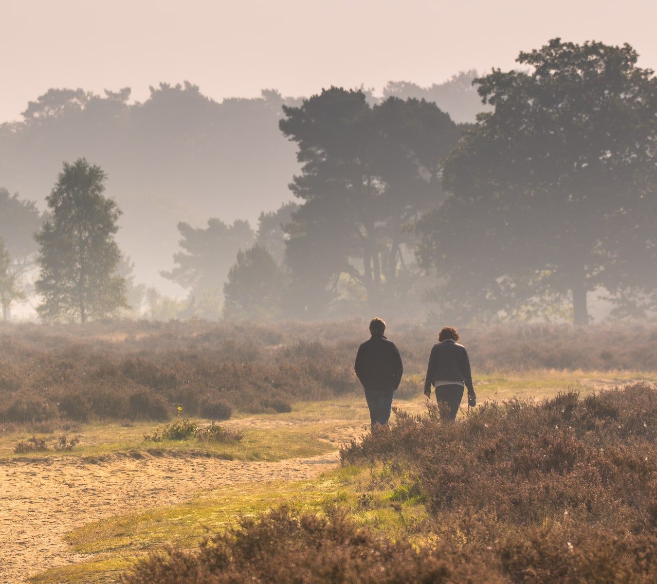 Twee mensen wandelen op een mistige heide.