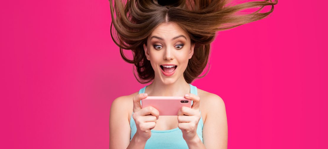 Vrouw met opgewonden blik kijkt naar smartphone.