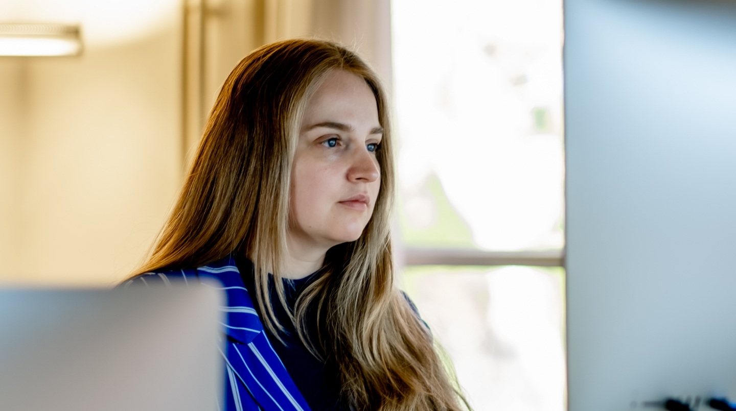 Vrouw kijkt geconcentreerd naar computerscherm in kantooromgeving.