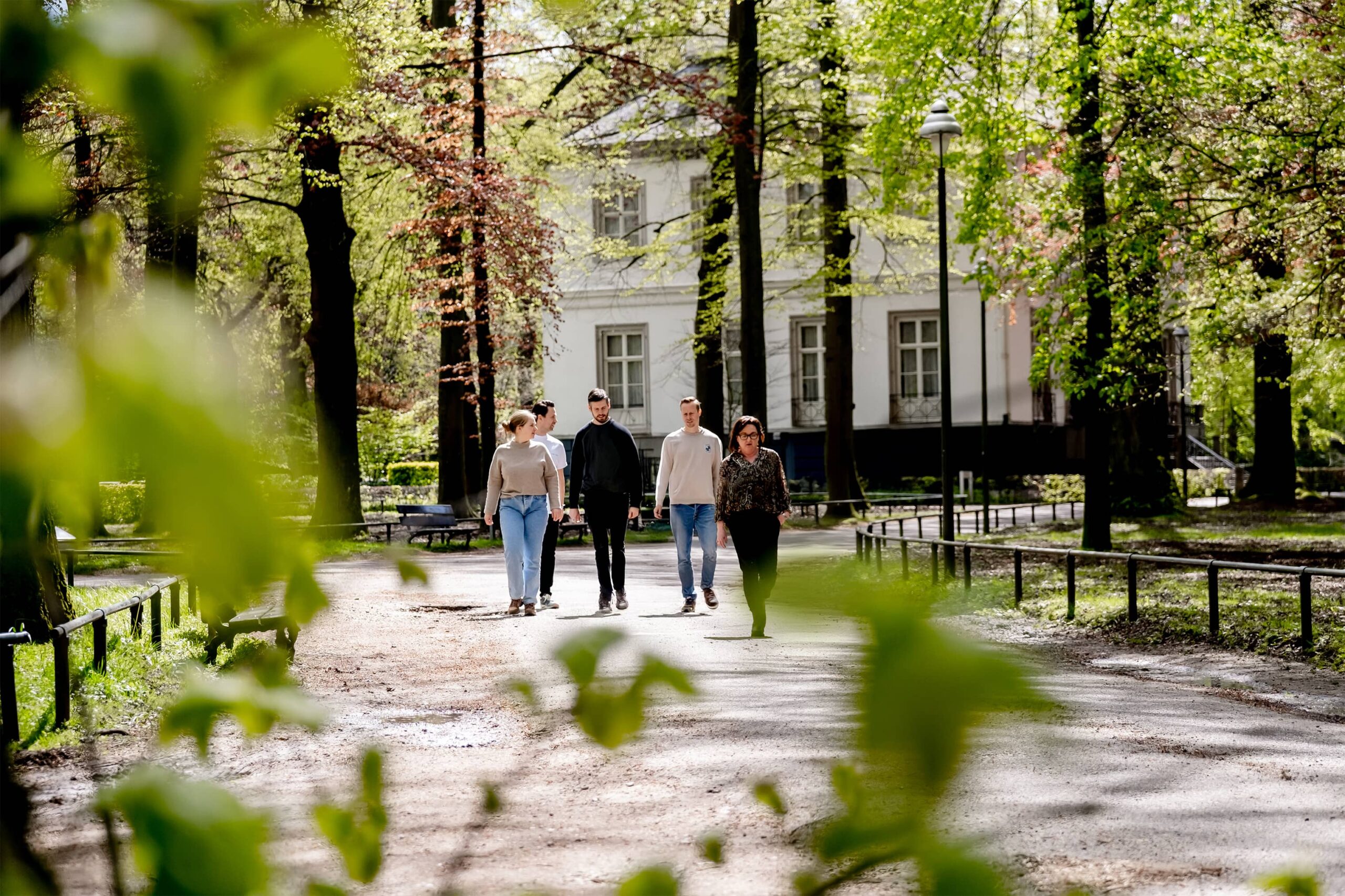 Collega's aan het wandelen tussen de bomen met op de achtergrond het pand.