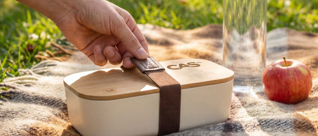 Productfoto van een lunchbox op een picknick kleed met een hand.